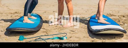 Giovane donna e uomo che si allenano per stare in piedi sul surf prima della prima lezione di surf BANNER, FORMATO LUNGO Foto Stock