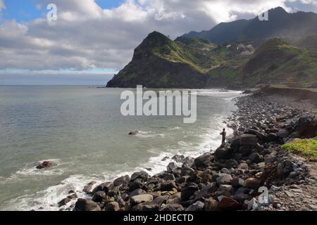 La costa intorno a Porto da Cruz, situato sulla costa nord dell'isola di Madeira, Portogallo, con la spiaggia di Maiata e un pescatore in primo piano Foto Stock