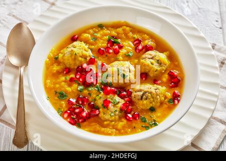 Anar di Ash-e, zuppa invernale di melagrana gialla in due pezzi con polpette, zuppa spessa, in una ciotola bianca con cucchiaio su un tavolo di legno bianco testurizzato, Foto Stock