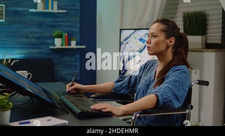 Fotografo non valido che lavora su software di ritocco con immagini e attrezzature professionali. Artista multimediale in sedia a rotelle che lavora con l'editing su un'applicazione moderna per la progettazione di immagini in studio Foto Stock