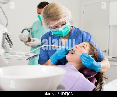 Dentista femminile che tratta il paziente della ragazza con assistente del maschio Foto Stock