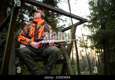 06 gennaio 2022, bassa Sassonia, Oerrel: Lars Niemeier, forester, siede sul sedile alto con la sua pistola durante una caccia di movimento in cui diversi cacciatori e cani sono coinvolti.durante una caccia regolare nel distretto forestale di Oerrel (Heidekreis), cinghiali sono anche da sparare. I campioni di sangue saranno prelevati dagli animali ed esaminati in laboratorio per individuare eventuali virus ASF. Foto: Philipp Schulze/dpa Foto Stock