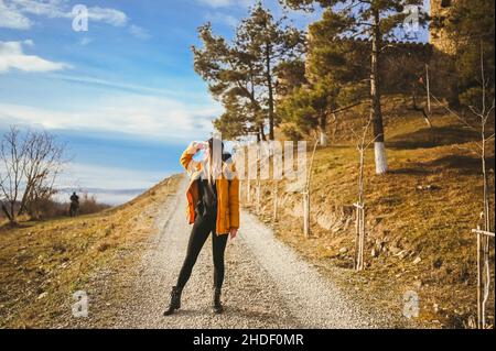 Giovane ragazza felice zaino in spalla donna turista viaggiando da solo e posando all'alba con nebbia sulla bella natura con montagne in autunno. Donna sorridente bionda in giacca gialla in giù che guarda in lontananza Foto Stock