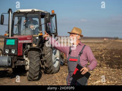 Agricoltore senior che mostra qualcosa per far maturare l'uomo nel trattore sul campo Foto Stock