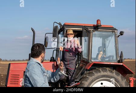 Agricoltore senior in piedi nel trattore e parlando con un uomo sul campo Foto Stock