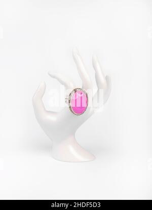Mano bianca in plastica con anello in argento e quarzo rosa su sfondo bianco Foto Stock