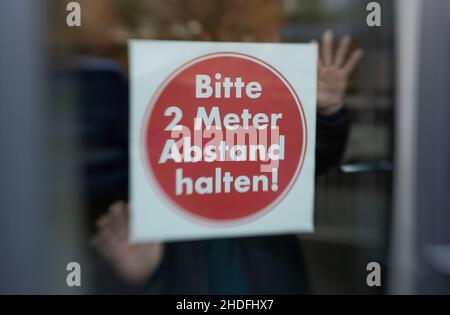 Bielefeld, Germania. 06th Jan 2022. Un janitor tiene un cartello "si prega di mantenere 2 metri di distanza" dalla finestra in una classe dalla Max Planck High School per il fotografo. Le attività scolastiche si trovano ad affrontare sfide importanti durante la crisi di Corona. Le misure comportamentali, le misure igieniche e protettive, la ventilazione, l'uso della protezione bocca-naso e i casi di quarantena devono essere gestiti ripetutamente. Credit: Friso Gentsch/dpa/Alamy Live News Foto Stock