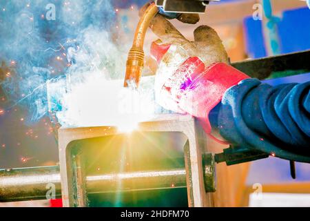 La saldatrice in indumenti protettivi utilizza una torcia ad alta potenza per tagliare attraverso un blocco di metallo Foto Stock