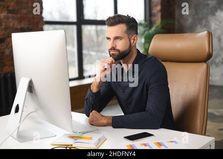 Uomo rilassato che lavora in un ufficio contemporaneo, digita sulla tastiera, siede su una comoda sedia, sentendosi sereno, godendo di aria condizionata fresca. Niente stress, niente fatica sul posto di lavoro Foto Stock