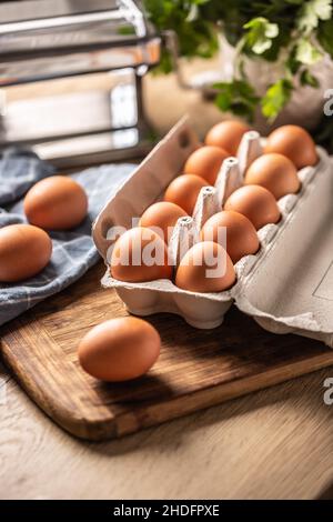 Uova in una scatola di cartone su un asse di legno in cucina. Foto Stock