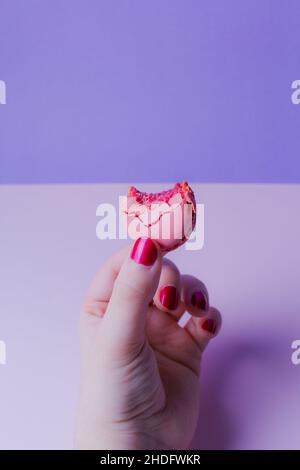 Mano femminile con dolce macaron morso su sfondo color pastello. Spazio di copia. Foto Stock