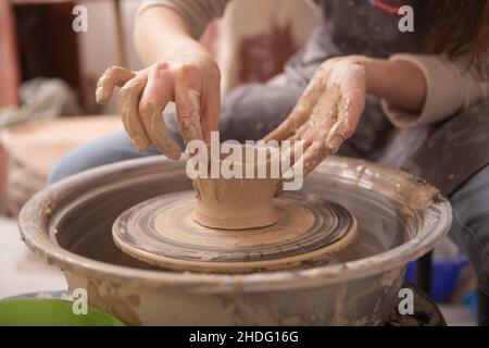 Primo piano in su colpo tagliato delle mani femminili che modellano l'argilla sulla ruota dei vasai Foto Stock
