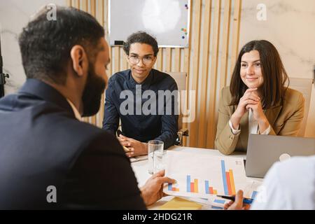 Oltre i dettagli. Gruppo di giovani uomini d'affari sicuri che discutono qualcosa mentre trascorrono tempo in ufficio. Bella brunette donna ufficio guardando i suoi colleghi durante la discussione Foto Stock