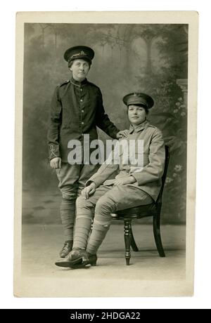 Cartolina originale del ritratto dello studio dell'era WW1 di 2 giovani donne vestite in uniformi del soldato. Forse le uniformi del loro ragazzo. La donna a sinistra indossa il badge con cappuccio dell'artiglieria reale e la donna a destra ne indossa uno del reggimento Wiltshire. Dallo studio di H A Aylward di Alton, Hampshire. Sul retro è scritto ' Agosto 1917, io e amico a Burkham'. Burkham è un borgo nella grande parrocchia di Bentworth nell'Hampshire orientale, Inghilterra e comprende una grande casa di campagna - Burkham House. 1917, REGNO UNITO Foto Stock