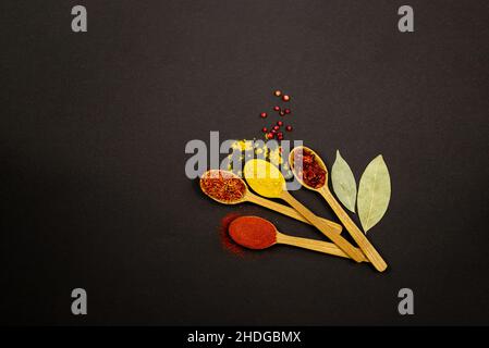 Su uno sfondo nero, sulla destra, ci sono quattro cucchiai di legno con spezie. Foto Stock