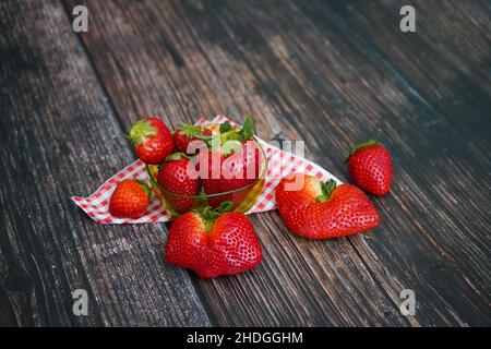 Fragole fresche biologiche con tovaglie rosse e bianche su un rustico tavolo in legno. Foto Stock