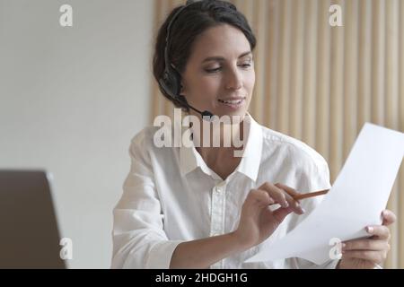 Una donna d'affari spagnola positiva in cuffia si siede alla scrivania per partecipare a una videoconferenza online con i partner Foto Stock