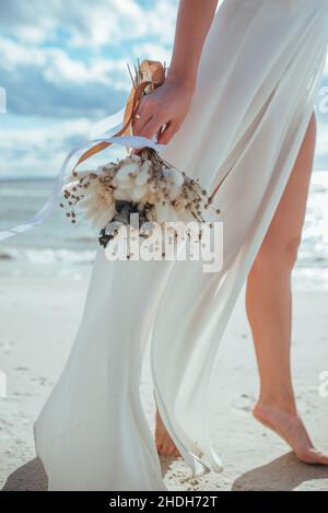 sposa tenera che tiene un bouquet di nozze nelle sue mani sullo sfondo del mare. Foto Stock