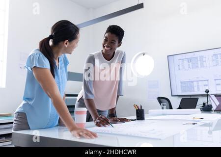 Le architetti femminili multirazziali sorridono mentre discutono sopra il progetto in riunione all'ufficio Foto Stock