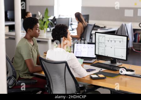 Architetti femminili multirazziali che discutono sopra il calcolatore con il blueprint in ufficio Foto Stock