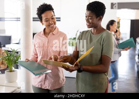 Sorridenti donne d'affari creative multirazziali discutere sopra la lima mentre camminano in ufficio Foto Stock