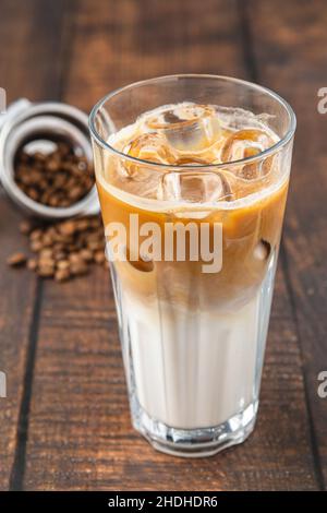 Una tazza di caffè Iced latte con cubetti di ghiaccio posti su un tavolo di legno in una caffetteria Foto Stock