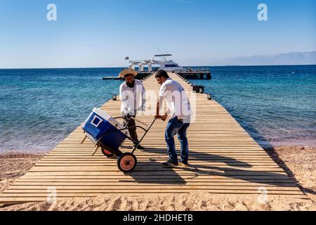 Due uomini su Un Jetty che prendono le forniture ad Una barca turistica al Berenice Beach Club, Aqaba, governatorato di Aqaba, Giordania. Foto Stock