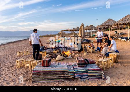 AC Gruppo di turisti si siede intorno Ad Un fuoco del campo sulla spiaggia al Berenice Beach Club, Aqaba, governatorato di Aqaba, Giordania. Foto Stock