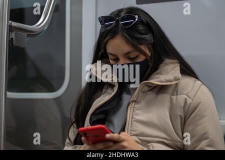 Bella donna che viaggia in metropolitana Buenos Aires con una maschera, tenendo il suo telefono cellulare rosso Foto Stock