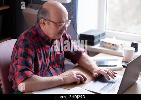 Uomo anziano con occhiali con computer portatile a casa che cerca in internet Foto Stock
