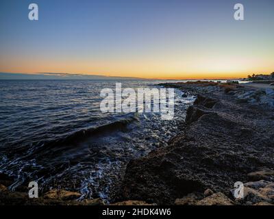 Vista panoramica delle onde che colpiscono la costa rocciosa sotto un cielo al tramonto - carta da parati Foto Stock