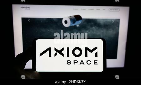 Persona che tiene il cellulare con il logo della società aerospaziale americana Axiom Space Inc. Sullo schermo di fronte al sito web aziendale. Mettere a fuoco sul display del telefono. Foto Stock