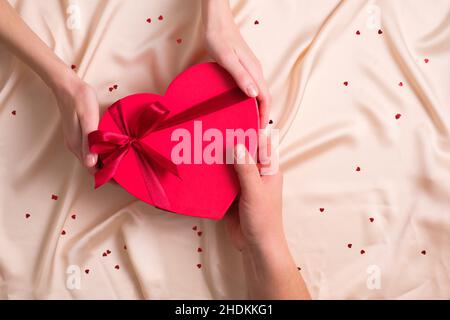 L'uomo dona una scatola di cioccolatini a forma di cuore all'amante. Disposizione piatta, vista dall'alto. Concetto di buon San Valentino. Foto Stock