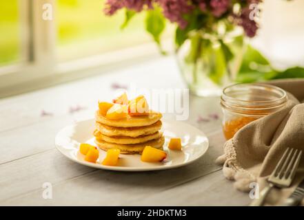 Pancake con pesca tagliata a colazione, persona in background Foto Stock