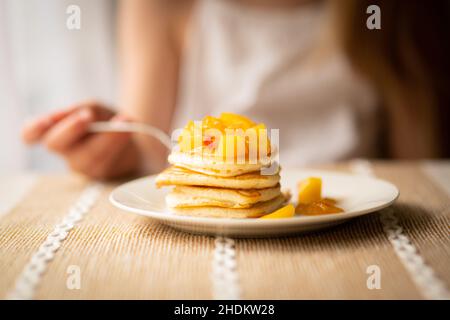 Pancake con pesca tagliata a colazione, persona in background Foto Stock