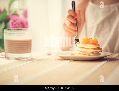 Pancake con pesca tagliata a colazione, persona in background Foto Stock