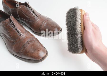 Studio girato di vecchio, stanco e poco graffiato cappuccio punta pizzo op scarpe oxford in marrone brunito, su sfondo bianco. Mano maschio destra che tiene a Foto Stock