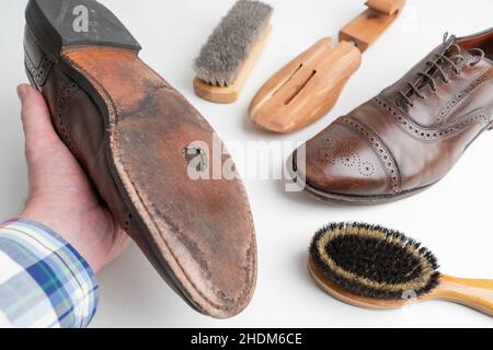 Foto studio di vecchio, stanco, poco graffiato cappellino punta pizzo op scarpe oxford in pelle di colore marrone brunito su sfondo bianco, nella mano sinistra maschile. Foro Foto Stock