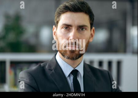 Primo piano di un business ritratto di successo intelligente influente barbuto caucasico uomo d'affari, top manager aziendale o specialista IT, vestito in abito, guardando la fotocamera, stand in ufficio moderno Foto Stock