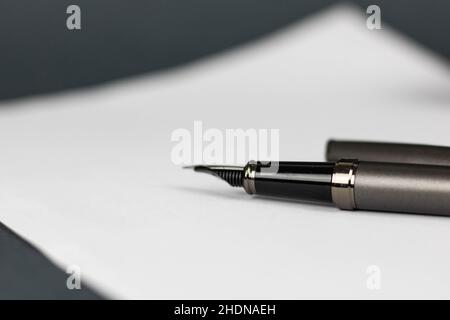 Macro di una penna nera con il cappuccio accanto ad essa adagiato su un pezzo di carta bianco con sfondo grigio Foto Stock