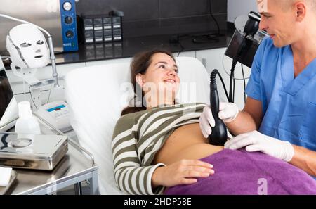 Cosmetologo che esegue la cavitazione ecografica del corpo procedura per il cliente femminile Foto Stock