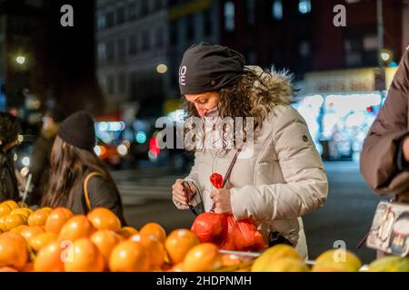 Una donna fa shopping in un mercato della frutta all'aperto a Chinatown di New York durante la pandemia Omicron onda COVID-19. Foto Stock