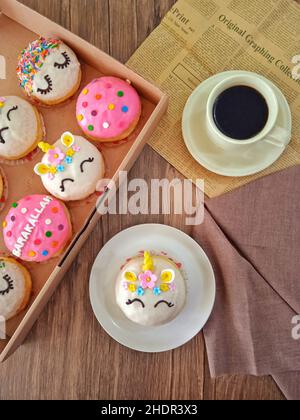 Unicorno ciambelle e una tazza di caffè su un tavolo di legno con tovagliolo e giornale Foto Stock