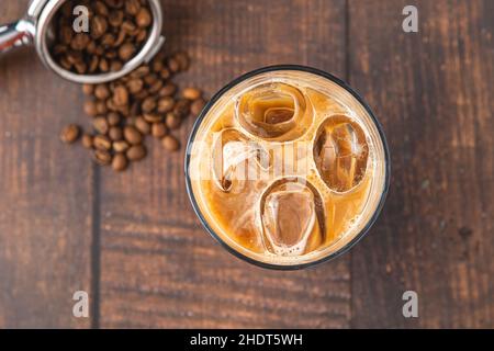 Una tazza di caffè Iced latte con cubetti di ghiaccio posti su un tavolo di legno in una caffetteria Foto Stock