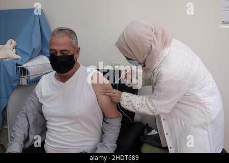 Gerusalemme, Israele. 6th Jan 2022. Un operatore sanitario arabo israeliano amministra il vaccino Pfizer-BioNTech COVID-19 a un anziano presso la clinica Leumit Health Services mentre Israele diventa il primo paese al mondo ad intraprendere una quarta campagna di vaccinazione COVID-19 il 6 gennaio 2022 a Gerusalemme, Israele. Israele ha iniziato a somministrare quarta dose di vaccino contro il coronavirus di Pfizer a persone di età superiore ai 60 anni e agli operatori sanitari, come parte degli sforzi per arginare il rapido aumento dei tassi di infezione causato dalla variante Omicron. Credit: Eddie Gerald/Alamy Live News Foto Stock