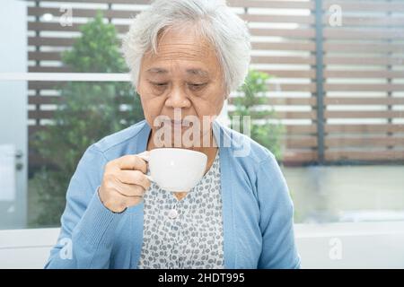 Donna anziana asiatica o anziana paziente che tiene la tazza e bere caffè al mattino a casa, sano e forte concetto medico Foto Stock