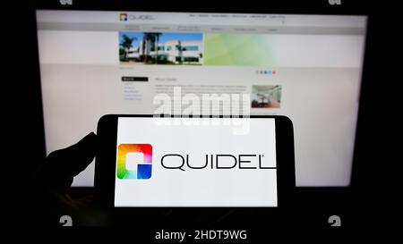 Persona che tiene lo smartphone con il logo della società di diagnostica statunitense Quidel Corporation sullo schermo di fronte al sito Web. Mettere a fuoco sul display del telefono. Foto Stock