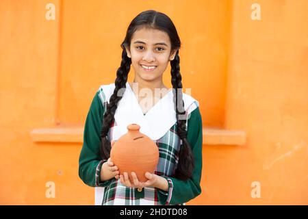 Ritratto di giovane ragazza indiana felice holidng scatola di denaro argilla o gullak in mano. Sorridendo capelli intrecciati femmina capretto che tiene tradizionale banca del piggy, risparmi il mon Foto Stock