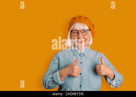 Ritratto di caucasica 50s donna che mostra pollici di buon umore in studio isolato su sfondo di colore arancione chiaro Foto Stock