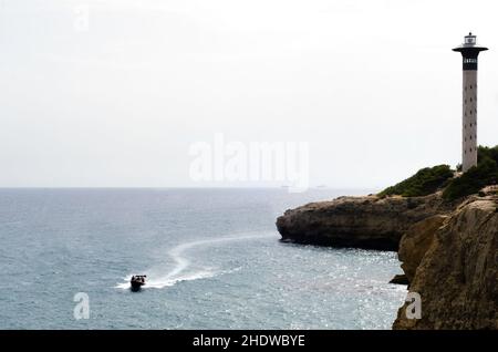 motoscafo ad alta velocità vicino alla costa. gruppo di giovani che si divertono in barca. giornata nuvolosa ma calda. Faro grande e alto. Due grandi Foto Stock